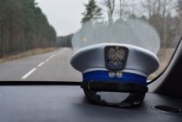 czapka policjanta wydziału ruchu drogowego leży na podszybiu radiowozu. Radiowóz jest w ruchu, z za szyby widać drogę