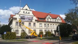 Pracownicy firmy za pomocą podnośnika koszowego montują na budynku Komendy Powiatowej Policji w Złotowie baner z okazji 100. rocznicy powołania Policji Państwowej. Baner Przedstawia po lewej policjantów pełniących służbę w 1919 roku i teraźniejszych funkcjonariuszy po prawej stronie baneru