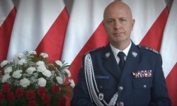 Komendant Główny Policji generalny inspektor Jarosław Szymczyk w umundurowaniu galowym stoi na tle flagi państwowej