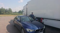 Policjant stoi przy nieoznakowanym radiowozie marki BMW