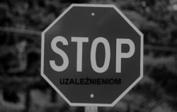 Znak drogowy stop. Pod umieszczonym napisem stop znajduje się słowo uzależnieniom. Zdjęcie czarno-białe