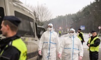 Policjanci stoi na tle pojazdu służbowego w jego kierunku idą dwie osoby ubrane w kombinezony ochronne