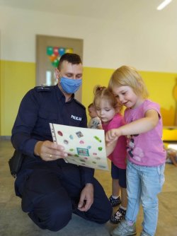 Policjant pokazuje planszę dwóm małym przedszkolakom