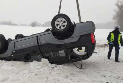 Samochód marki hyundai leży na dachu na poboczu zaśnieżonej drogi. po jego lewej stronie stoi policjant.