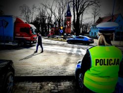 Policjantka ruchu drogowego stoi przy oznakowanym przejściu dla pieszych i obserwuje zachowania kierujących wobec pieszych