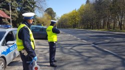 Policjanci dokonują pomiaru prędkości w miejscowości Jastrowie. Funkcjonariusze ruchu drogowego stoją przy drodze krajowej nr 11 ubrani w umundurowanie służbowe i żółte kamizeli w tle widoczny policyjny radiowóz oznakowany marki kia