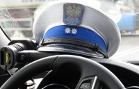 Czapka policjanta ruchu drogowego leży na podszybiu radiowozu oznakowanego. Przez szybę widoczna droga na której policjanci pełnią służbę.